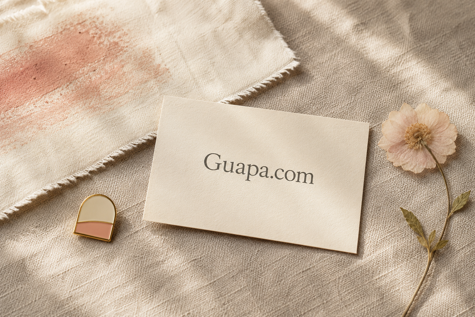 Cotton swatch, cream card, and enamel pin showing Guapa.com on linen